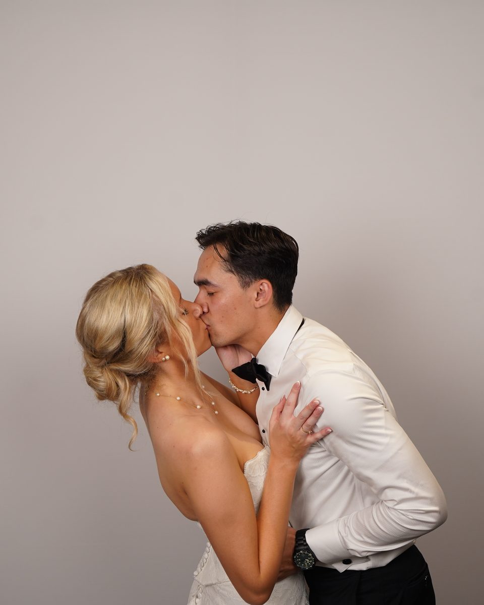 A couple standing close in front of the white tension-fabric backdrop, lit evenly from the front