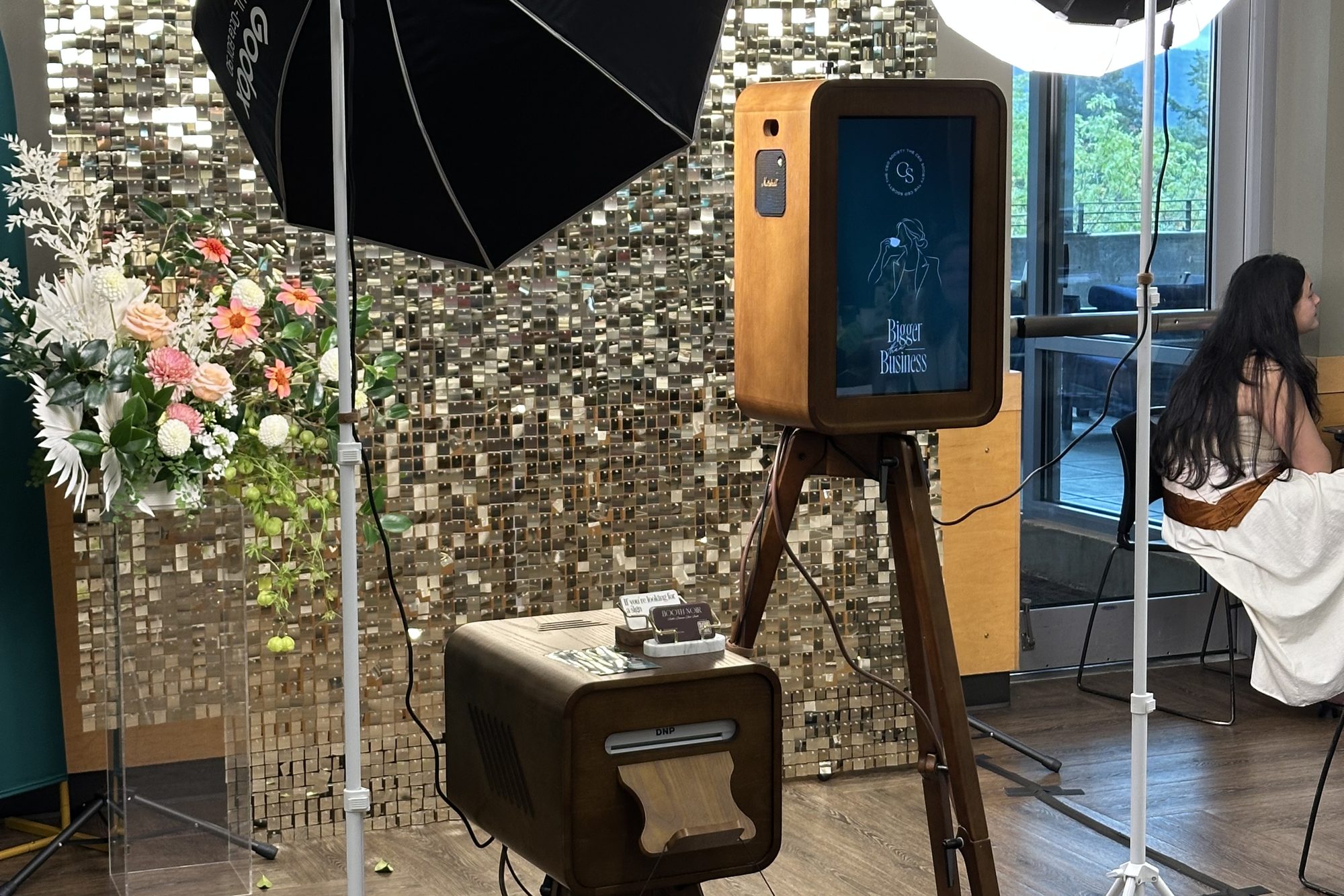The booth on its stand beside the print station, a sequin wall behind and flowers to one side, at the Mercer Island Community & Event Center