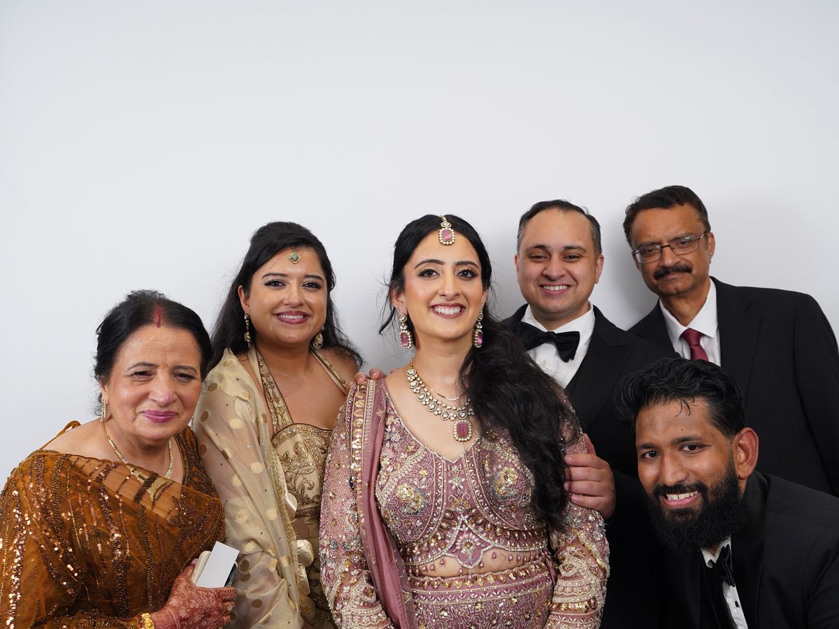 The bride with family in front of the white backdrop, in gold, maroon, and black